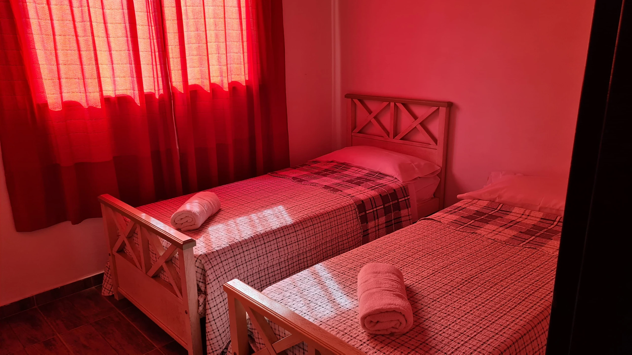 Dos camas individuales con toallas preparadas junto a cortinas rojas.
