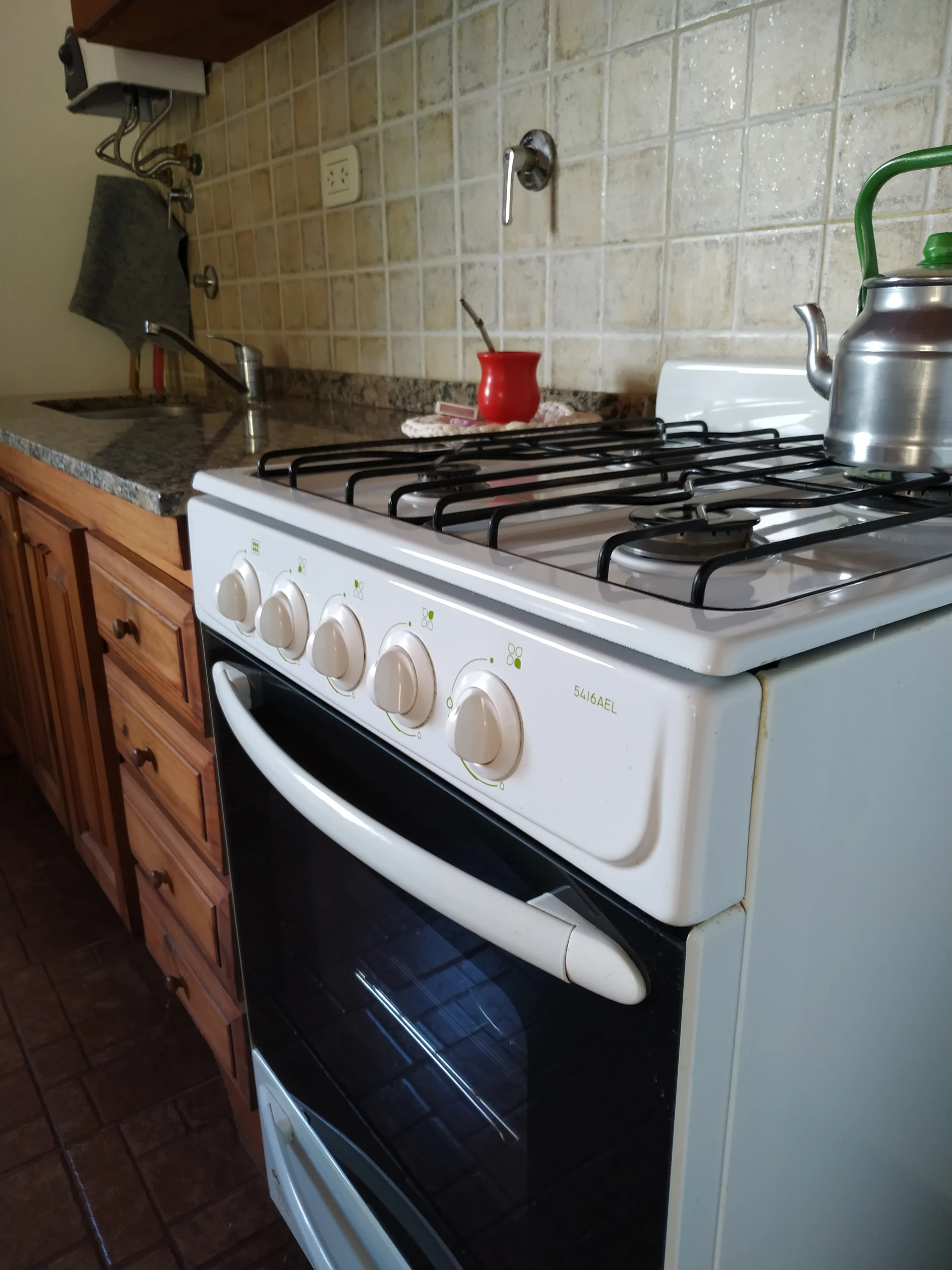 Cocina a gas con horno, una pava y un mate sobre las hornallas.