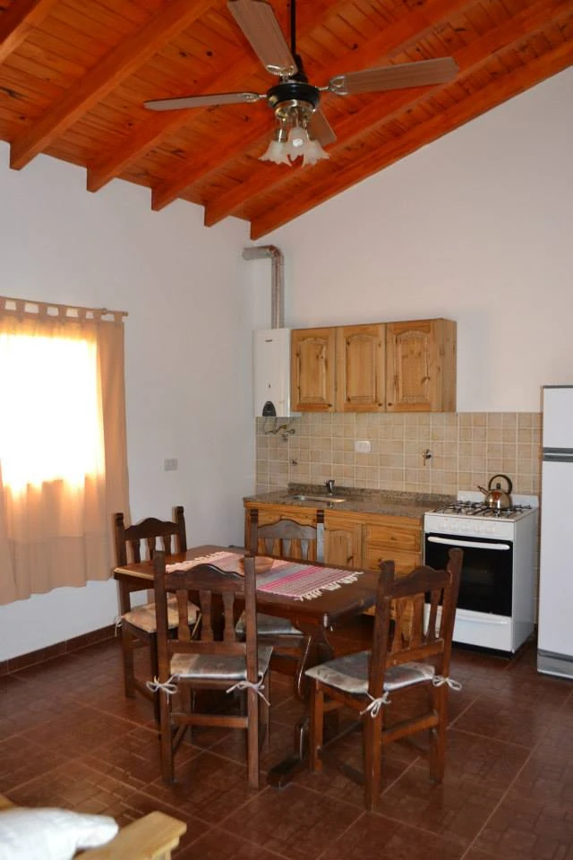Comedor con mesa de madera junto a la cocina, bajo techo con ventilador.