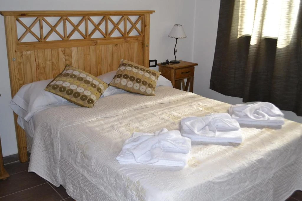Cama matrimonial con almohadones y toallas junto a una ventana con cortinas oscuras.