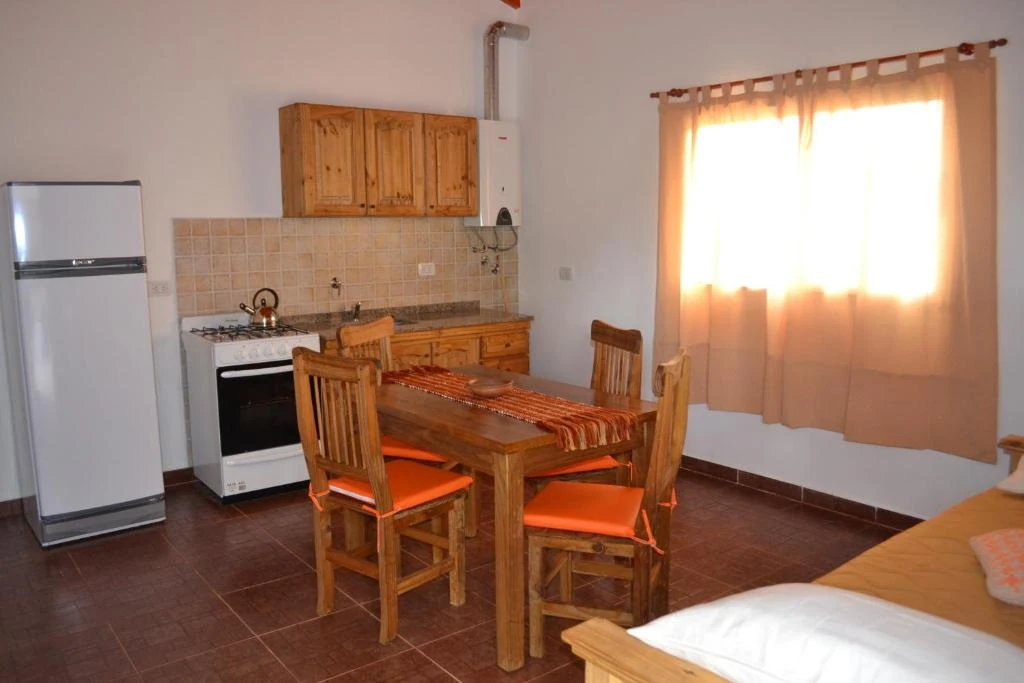 Mesa y sillas junto a la ventana, frente a la cocina con horno y heladera.