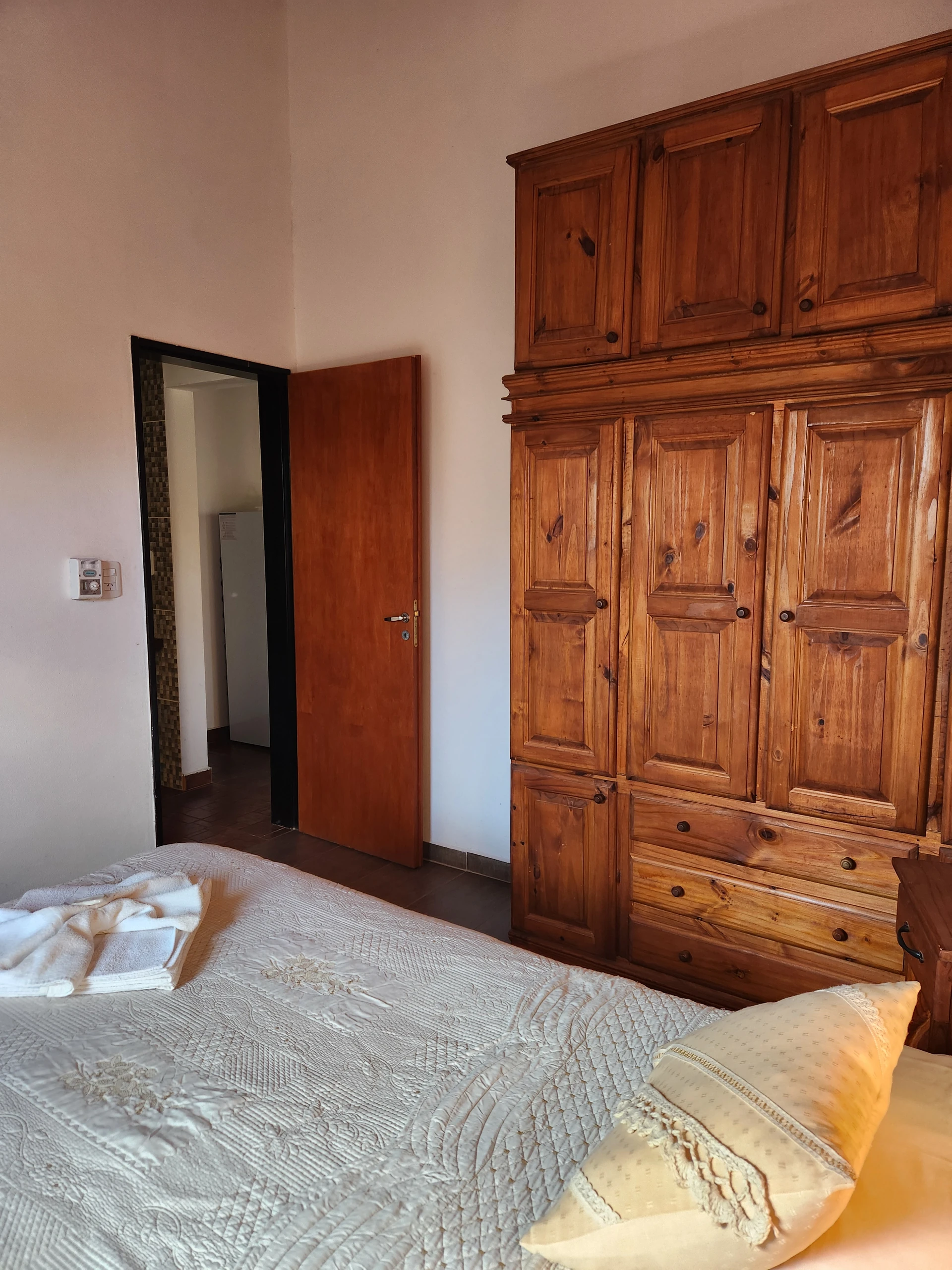 Placard de madera y puerta abierta junto a una cama con toallas.