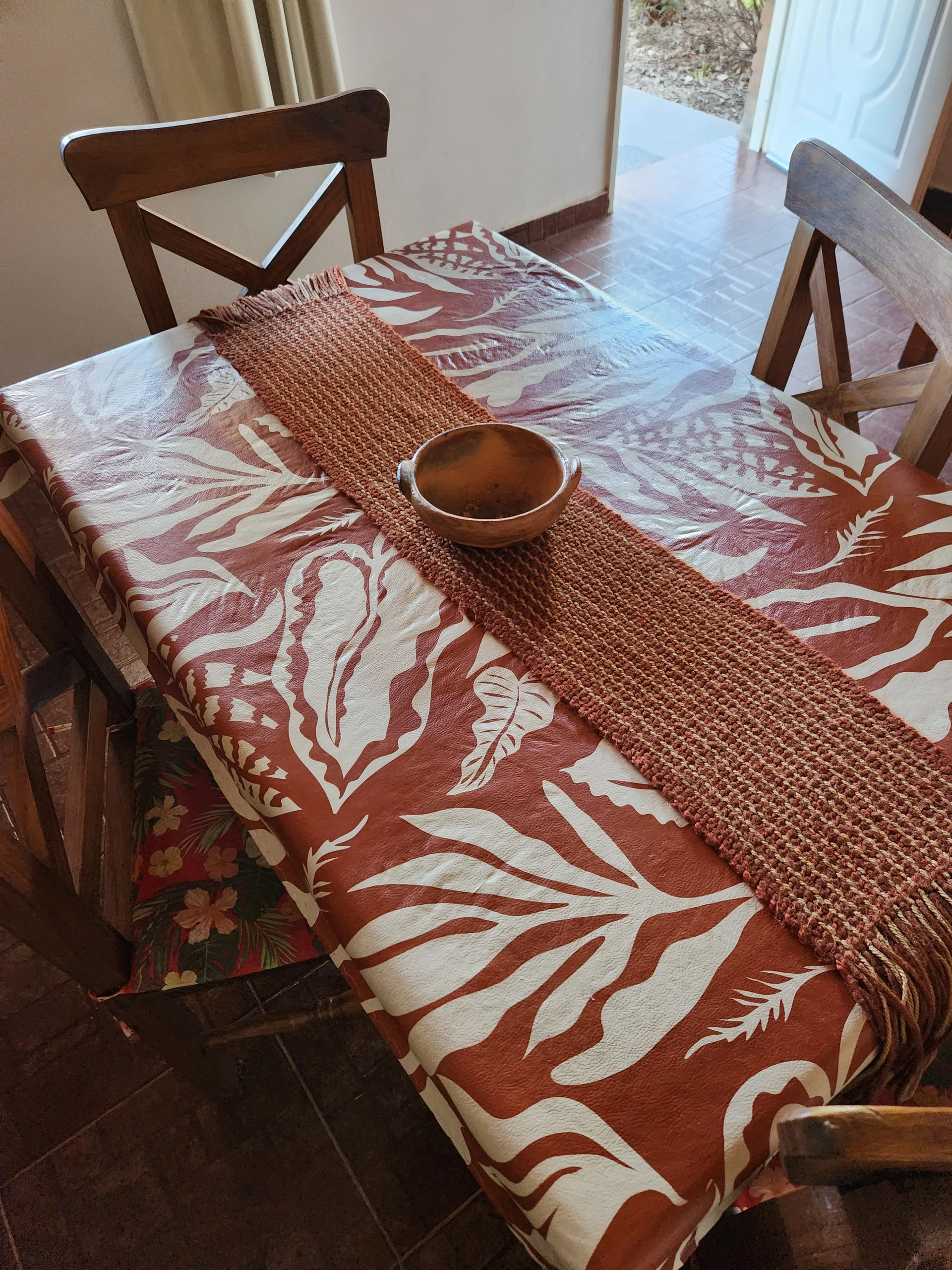 Mesa con mantel estampado y sillas de madera junto a una ventana.