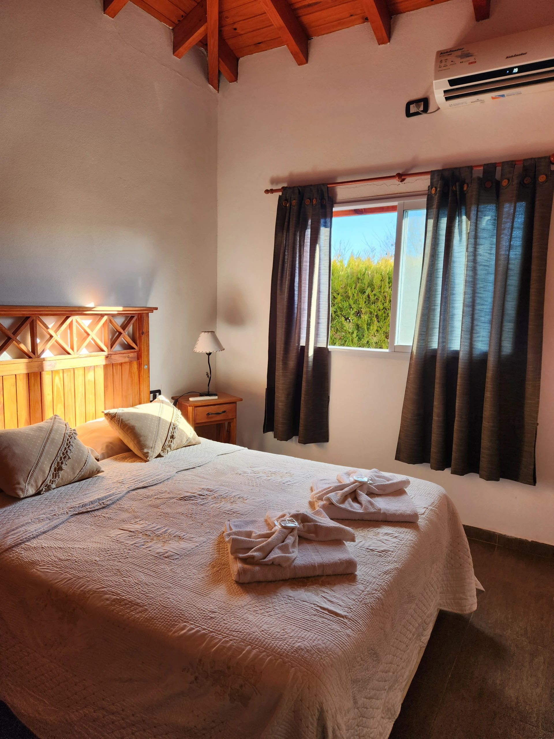 Cama matrimonial con toallas frente a una ventana con cortinas de varios colores.