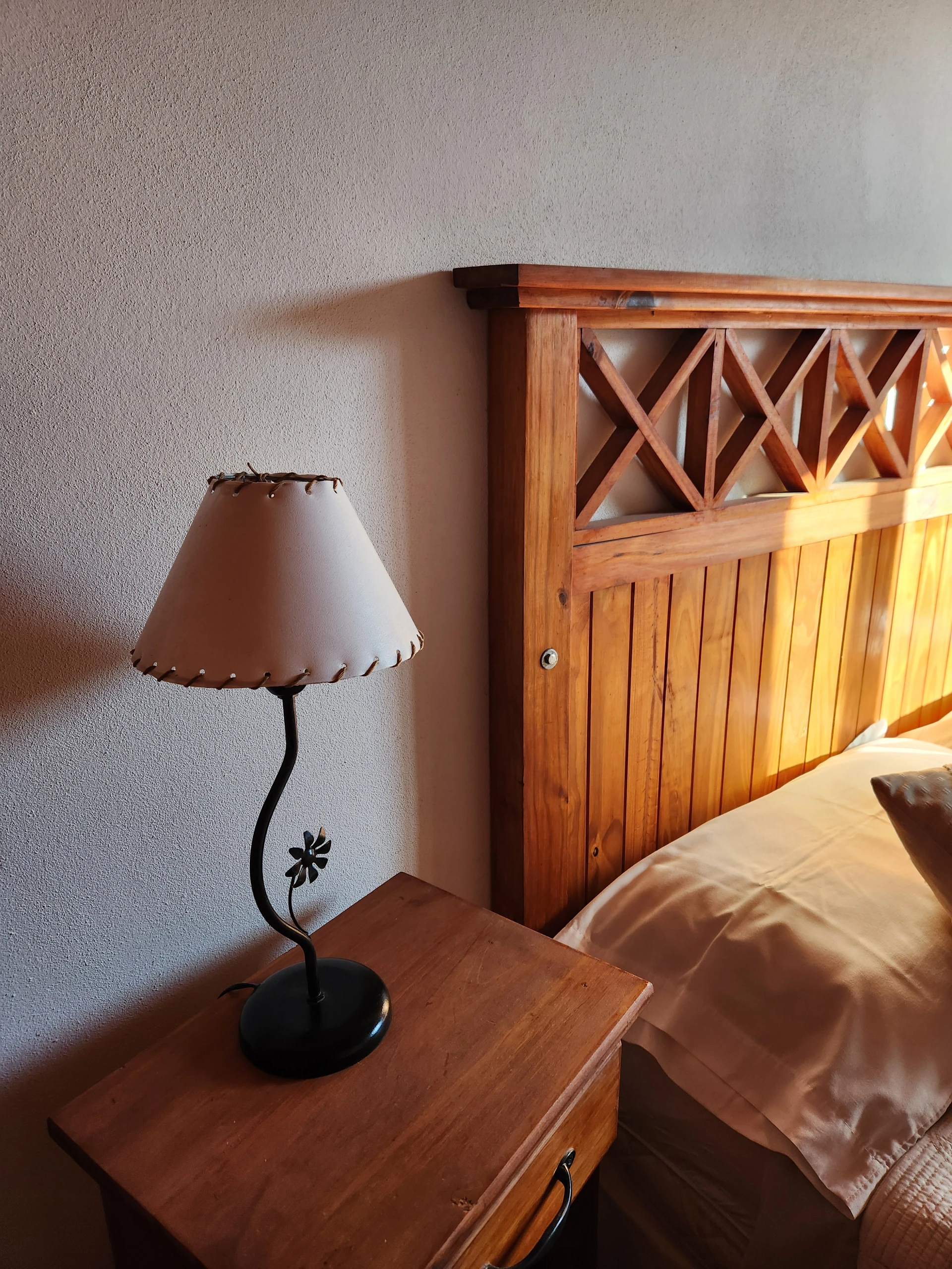 Lámpara sobre una mesa de luz junto al respaldo de madera de la cama.